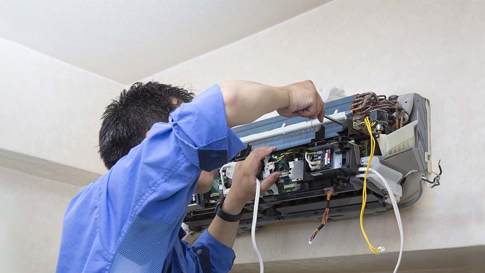 Aircon technician troubleshooting a faulty aircon unit with diagnostic tools in Singapore